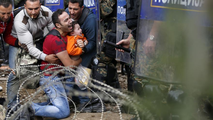 Dos hombres ayudan a un compañero que sostiene un niño ante la ante las fuerzas especiales macedonias mientras esperan el permiso policial para cruzar de Grecia a Macedonia. / Darko Vojinovic - AP