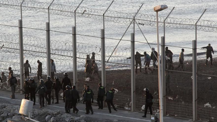 Policía española e inmigrantes a ambos lado de la valla de Ceuta, junto al agua (EFE)