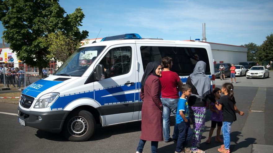Refugiados parados al lado de un vehículo de la policía antes de una visita de la canciller alemana Angela Merkel al alojamiento de refugiados en Heidenau, Alemania, 26 de agosto de 2015/ Foto: Arno Burgi - AP