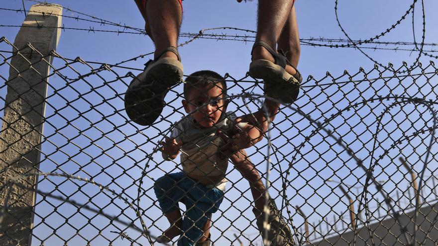 Ayudan a cruzar la valla que divide Siria y Turquía a un niño, al que llevan en volandas al lado turco en la zona de Akcakale, este 14 de junio. / (AP Photo/Lefteris Pitarakis). 