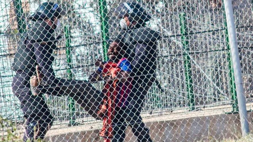 Dos agentes devuelven a un inmigrante a Marruecos tras el intento de salto del 1 de mayo de 2014. / Foto:José Palazón.