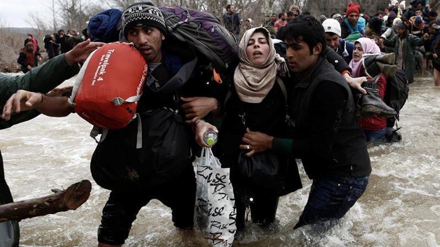 Un grupo de refugiados ayudándose a cruzar un río para pasar la frontera entre Grecia y Macedonia / EFE