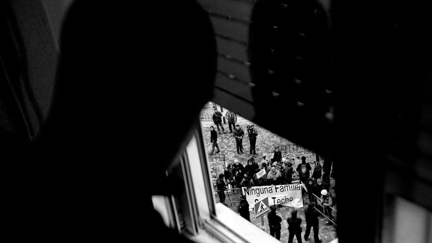 Un hombre observa por la ventana el despliegue policial y la concentración de protesta organizadas antes de su desahucio