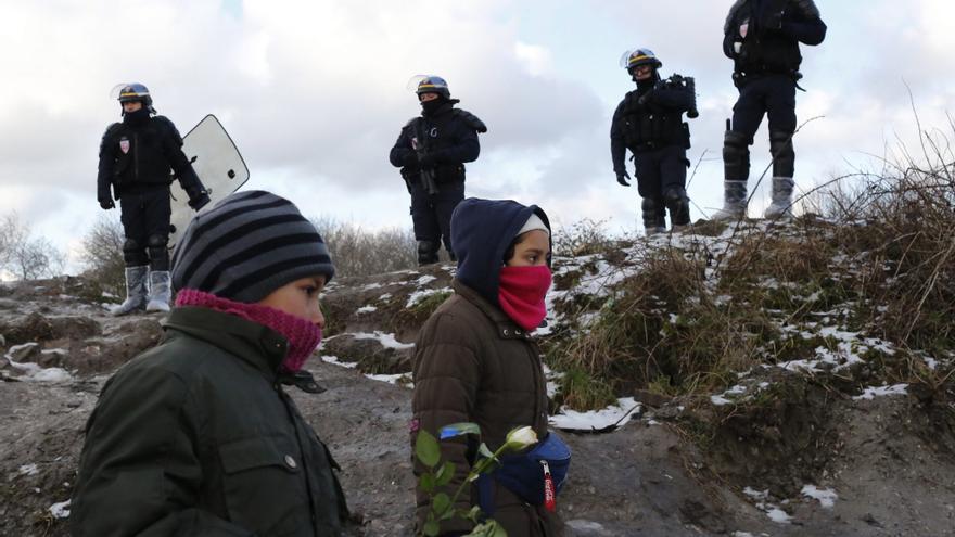Dos niños pequeños en el campamento de refugiados de Calais, ante la mirada de unos policías.  