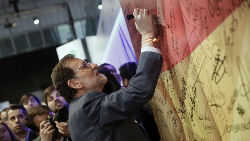 El presidente del Gobierno y líder del PP, Mariano Rajoy, firma en una bandera española a su llegada a la segunda jornada del XVIII Congreso nacional del partido en la Caja Mágica, el 11 de febrero de 2017